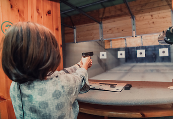 Image showing A woman practices shooting a pistol in a shooting range while wearing protective headphones