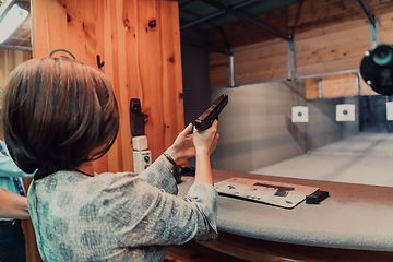 Image showing A woman practices shooting a pistol in a shooting range while wearing protective headphones