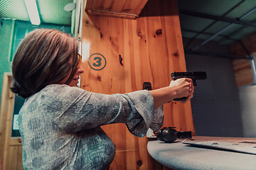 Image showing A woman practices shooting a pistol in a shooting range while wearing protective headphones