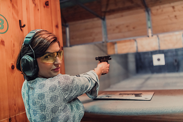 Image showing A woman practices shooting a pistol in a shooting range while wearing protective headphones