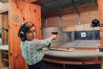 Image showing A woman practices shooting a pistol in a shooting range while wearing protective headphones