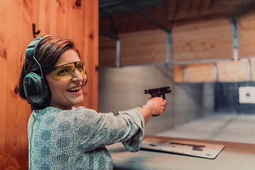 Image showing A woman practices shooting a pistol in a shooting range while wearing protective headphones