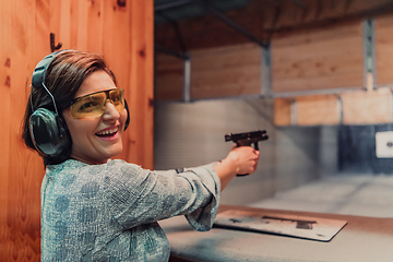 Image showing A woman practices shooting a pistol in a shooting range while wearing protective headphones