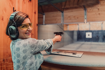 Image showing A woman practices shooting a pistol in a shooting range while wearing protective headphones