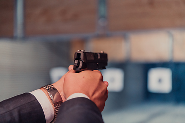 Image showing A man practices shooting a pistol in a shooting range while wearing protective headphones