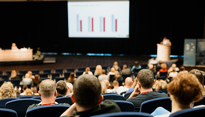 Image showing Speaker giving a talk in conference hall at business event. Rear view of unrecognizable people in audience at the conference hall. Business and entrepreneurship concept.