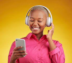 Image showing Happy, phone and black woman with music headphones in studio for streaming, track or selection on yellow background. Radio, podcast and African lady online with smartphone for audio subscription app