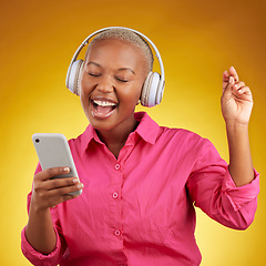 Image showing Phone, headphones for music and black woman singing along to radio, sound or podcast in studio isolated on a yellow background. Happy, audio and African person listen, streaming and dance with energy