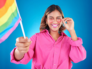 Image showing Woman, lgbtq and pride flag in studio portrait, sunglasses or icon with smile for human rights by blue background. Gen z girl, young lesbian student and wave sign for solidarity, freedom or inclusion