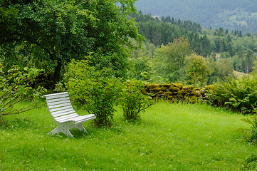 Image showing white bench in old garden with mossy stone fence