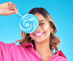 Image showing Woman, lollipop eye and studio portrait for eating, sweets and comic smile with food by blue background. Girl, student or young fashion model with candy, beauty and funny with sugar for dessert snack