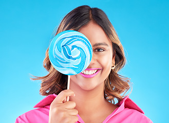 Image showing Portrait, lollipop or happy woman on a blue background in studio with positive, sugar or cheerful smile. Colorful sweets, hungry or face of Indian girl eating a giant snack, treats or candy with joy