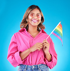 Image showing Woman, smile and pride flag in studio portrait with fashion, sunglasses and sign for human rights by blue background. Gen z girl, lesbian student and happy at protest, support and freedom for lgbtq