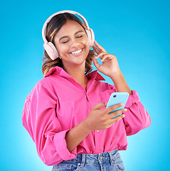 Image showing Phone, music and headphones with a woman in studio on a blue background, listening to the radio. Mobile, smile and a happy young female person streaming audio to relax for wellness or freedom