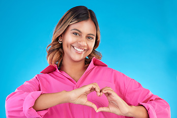 Image showing Woman, heart shape and smile portrait in studio for love, fashion or happiness. Happy person show sign with hands, icon or emoji for support, kindness and motivation for charity on a blue background