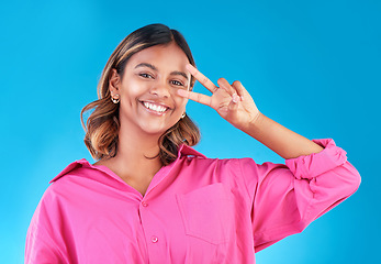 Image showing Smile, happy and peace sign with portrait of woman in studio for support, gen z and emoji. Motivation, kindness and winner with face of person on blue background for v icon, positive and symbol