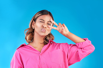 Image showing Wink, kiss and peace sign with portrait of woman in studio for support, gen z and emoji. Motivation, kindness and winner with face of person on blue background for v icon, positive and symbol