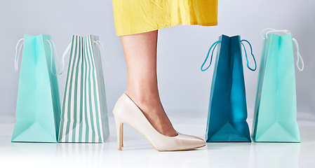 Image showing Shopping bag, shoes and a woman in studio for fashion sale, promotion or retail discount. Feet of a female model or customer on a white background advertising commerce offer, high heels or gift