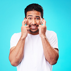 Image showing Fear, hope and portrait of man fingers crossed, anxiety or nervous due to crisis or stress isolated in studio blue background. Worry, suspense and young male person hands in face for mistake reaction