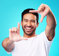 Image showing Happy, hand frame and portrait of a man for a selfie, creative aesthetic or advertising photography. Smile, laughing and face of an Asian person with a gesture for a photo on a blue background