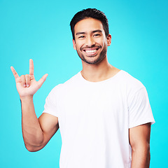 Image showing Man, horns and love in studio portrait with smile, kindness and sign language by blue background. Young guy, student and happy with icon, emoji and hand with care, romance or vote with white t-shirt