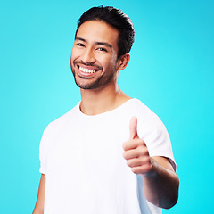 Image showing Smile, thumbs up and portrait of a man in a studio with a satisfaction sign or expression. Happy, emoji and young Indian male model with an agreement hand gesture isolated by a blue background.