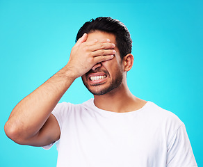 Image showing Scared, covering eyes and a man on a blue background for fear, anxiety or angry with a problem. Mental health, fail and a person with hands on face while frustrated and isolated on a studio backdrop