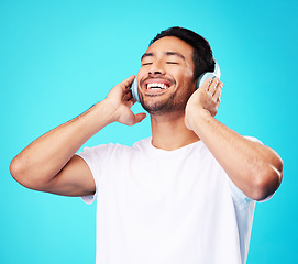 Image showing Music, headphones and happy man listening in studio isolated on a blue background. Radio, smile and person with audio, sound or hearing podcast, jazz or media for hip hop with eyes closed for freedom