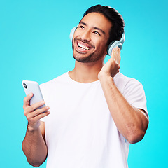 Image showing Music, headphones and Asian man with phone for listening in studio isolated on a blue background. Radio, smile and person with audio, sound and hearing podcast, jazz or media for hip hop with mobile