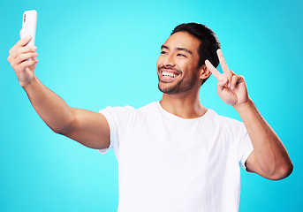 Image showing Happy, peace sign and a man with a phone on a blue background for communication or social media. Smile, contact and a male influencer with an emoji hand and a mobile while live streaming in studio