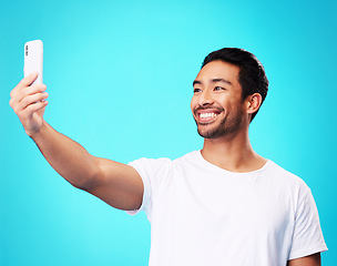 Image showing Asian man, selfie and smile in studio for social media post, web chat and excited by blue background. Young guy, student or influencer with memory, profile picture and photography for update on blog