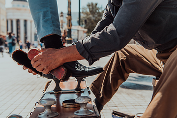 Image showing An old man hand polishing and painting a black shoe at street