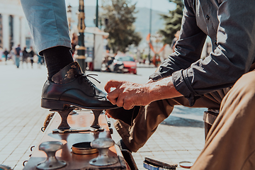 Image showing An old man hand polishing and painting a black shoe at street