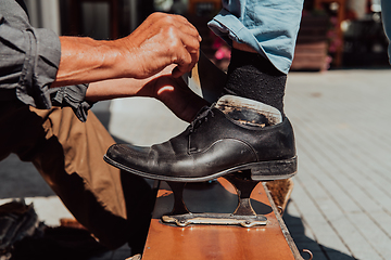 Image showing An old man hand polishing and painting a black shoe at street