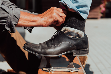 Image showing An old man hand polishing and painting a black shoe at street