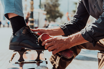 Image showing An old man hand polishing and painting a black shoe at street