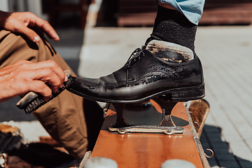 Image showing An old man hand polishing and painting a black shoe at street