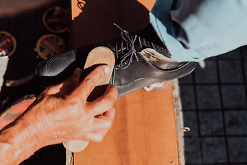 Image showing An old man hand polishing and painting a black shoe at street