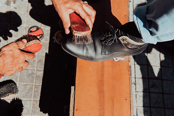 Image showing An old man hand polishing and painting a black shoe at street