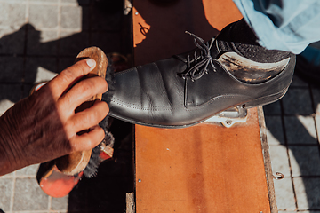 Image showing An old man hand polishing and painting a black shoe at street