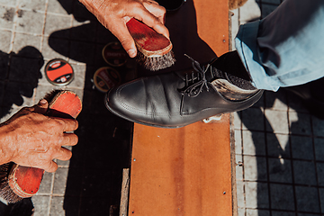 Image showing An old man hand polishing and painting a black shoe at street