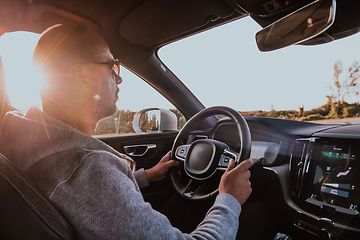 Image showing A man with a sunglasses driving a car at sunset. The concept of car travel