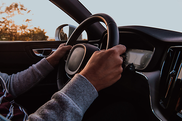 Image showing Close up man hand driving a car at sunset. The concept of car travel