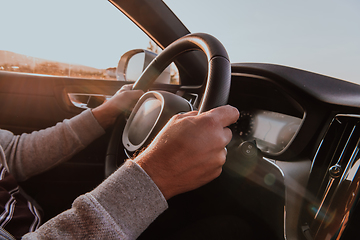 Image showing Close up man hand driving a car at sunset. The concept of car travel