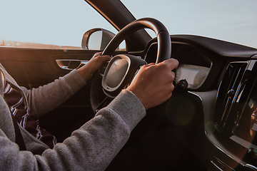 Image showing Close up man hand driving a car at sunset. The concept of car travel