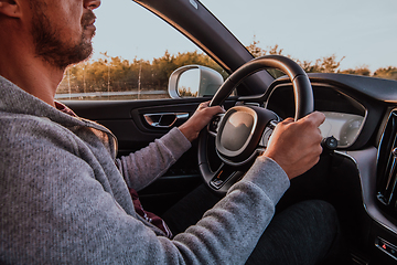 Image showing Close up man hand driving a car at sunset. The concept of car travel