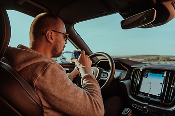 Image showing A tired man drinking acoffee while driving a car at sunset. Tired travel and long drive