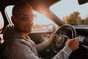 Image showing A man with a sunglasses driving a car at sunset. The concept of car travel