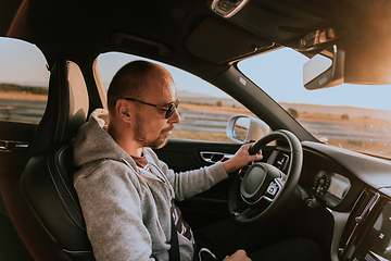 Image showing A man with a sunglasses driving a car at sunset. The concept of car travel