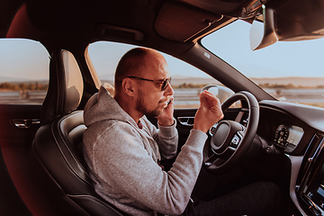 Image showing A man with a sunglasses driving a car and talking on smartphone at sunset. The concept of car travel